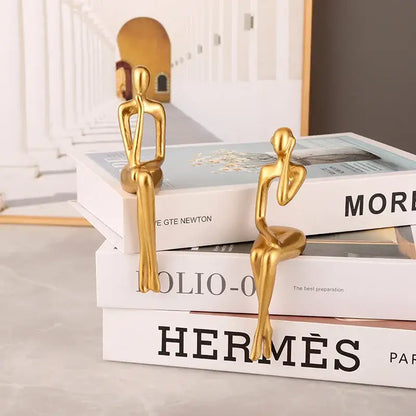 Two sleek gold-colored minimalist abstract figurines sit atop stacked books in the decorbites abstract figurines set