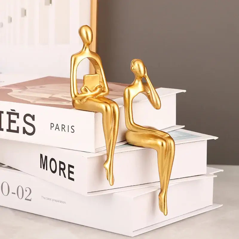 Two sleek golden decorbites abstract figurines seated on stacked books in modern art sculpture set for home and office