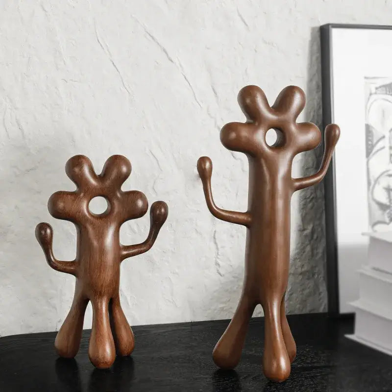 Two brown wooden decorbites abstract flower man figurines with rounded shapes and central torso holes for home decor