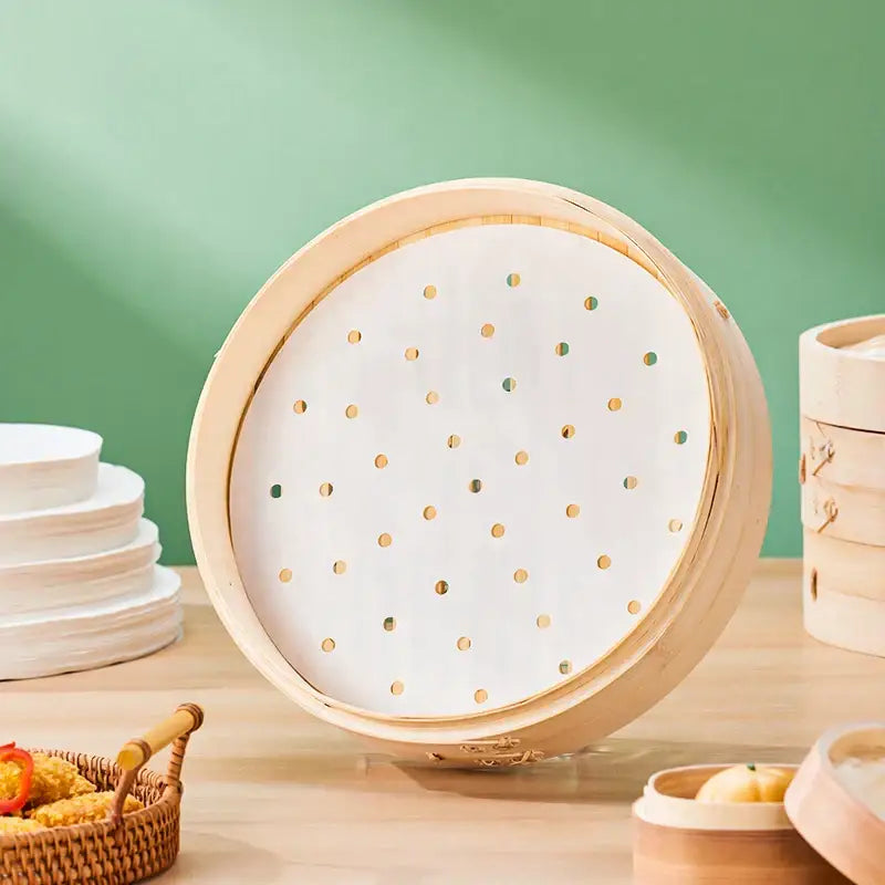 A round bamboo steamer basket with white perforated decorbites™ air fryer steamer papers featuring golden dots