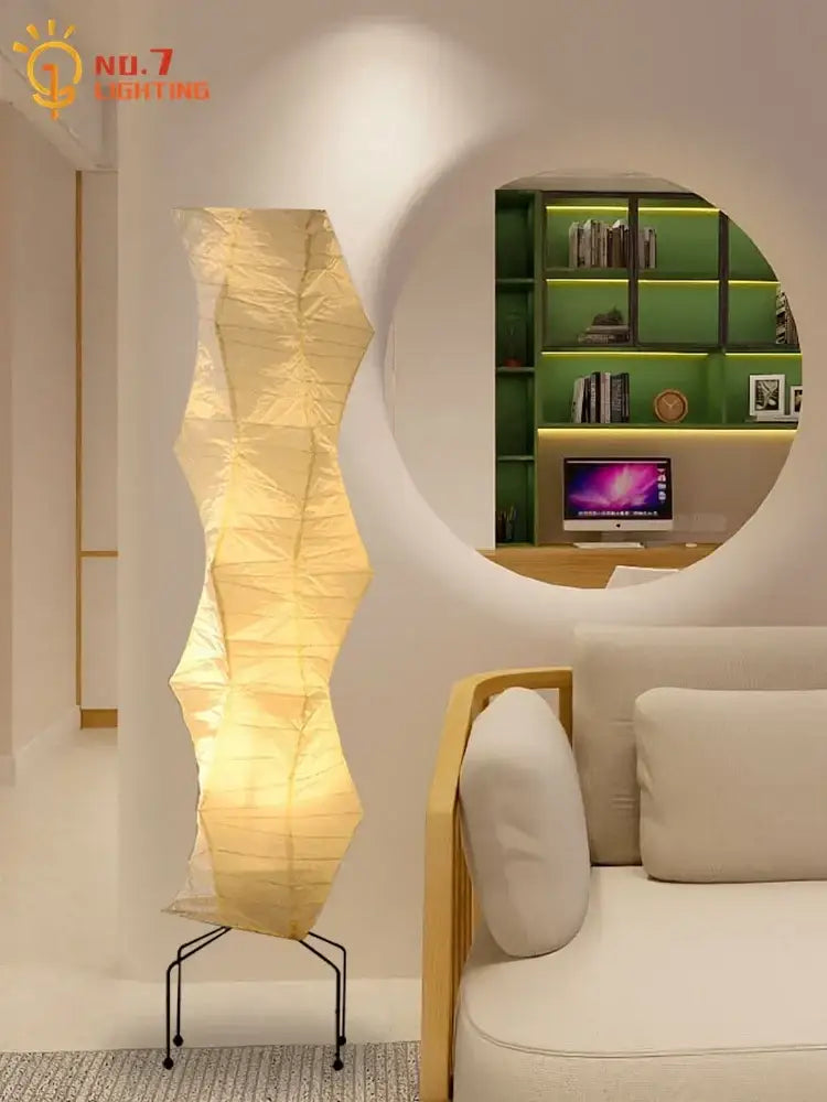 A tall slender floor lamp with a warm golden glow and akari noguchi rice paper shade supported by thin black metal legs