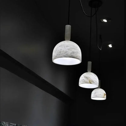 Three elegant white marble alabaster pendant lights with cylindrical necks hang in a modern living room setting