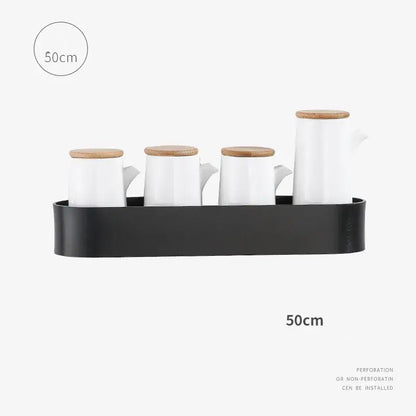 Set of white ceramic oil and vinegar dispensers with bamboo lids on a black tray beside an aluminum bathroom shelf with towel bar