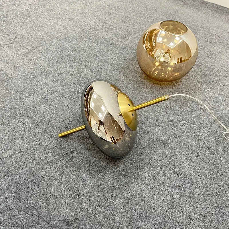 Decorbites amber glass chandelier featuring two spherical lampshades in reflective silver and warm amber hues on gold stems