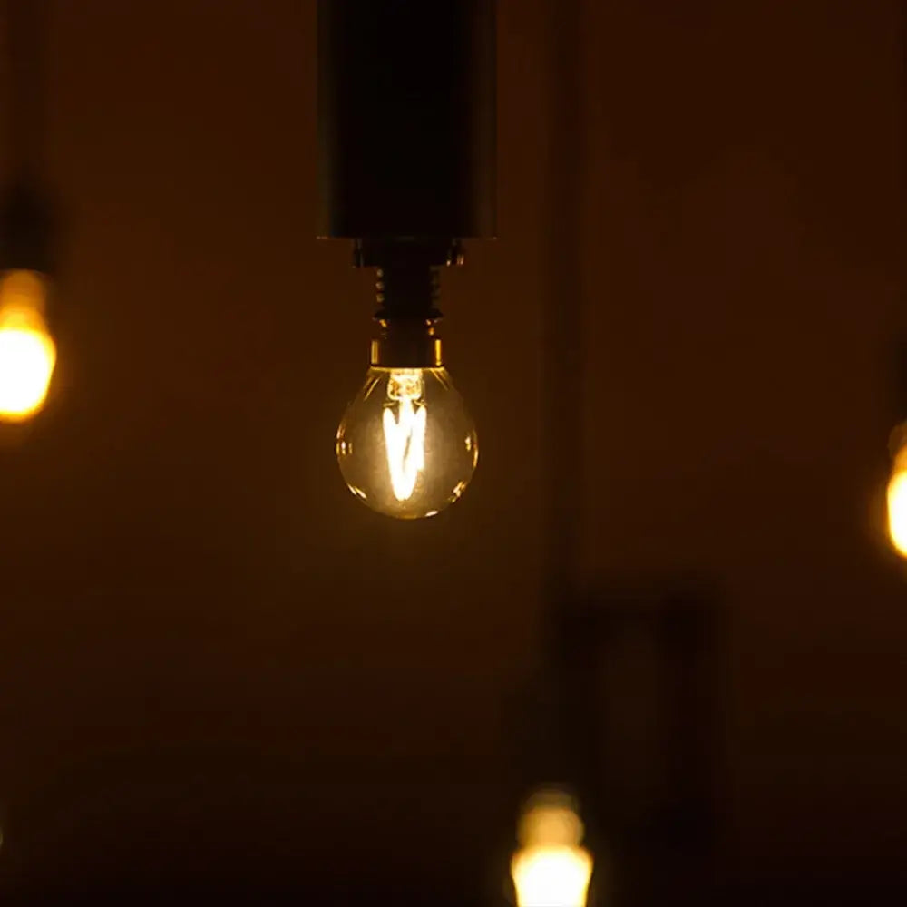 Warmly glowing DecorBites™ amber glass led filament globe bulb with clear glass and visible filament in dark metal fixture