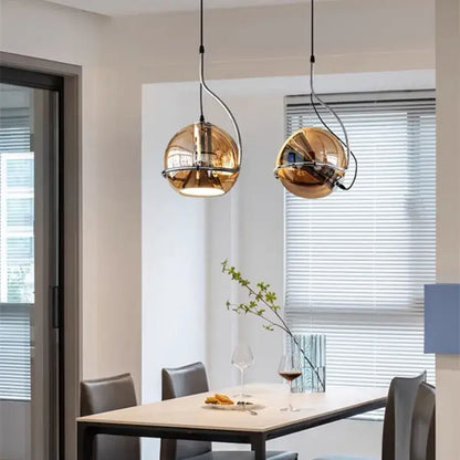 Two spherical gold decorbites amber glass pendant lights with reflective finish hanging above a dining table