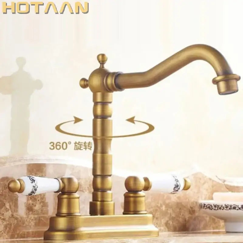 Antique brass dual basin faucet with ornate segmented spout and white ceramic handles featuring black floral detailing