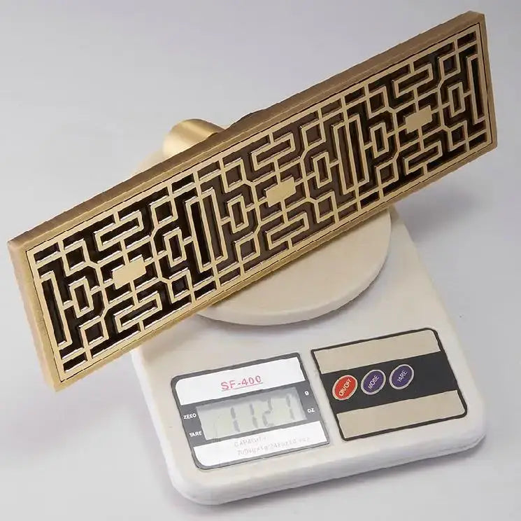 Decorbites™ antique brass linear shower floor drain with brass rectangular vent and intricate geometric lattice design