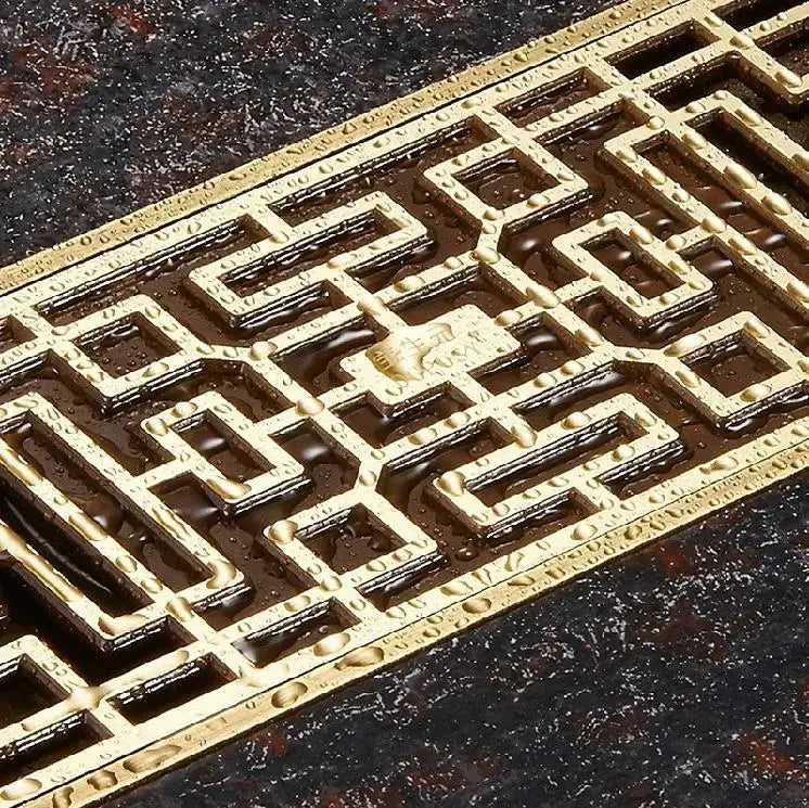 DecorBites antique brass linear shower floor drain with golden brass vent cover featuring intricate geometric lattice design