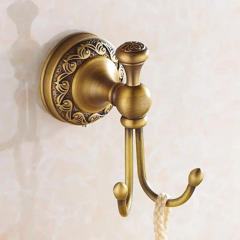 Antique brass robe hooks with ornate scrollwork design and a rope hanging from the lower hook by DecorBites™