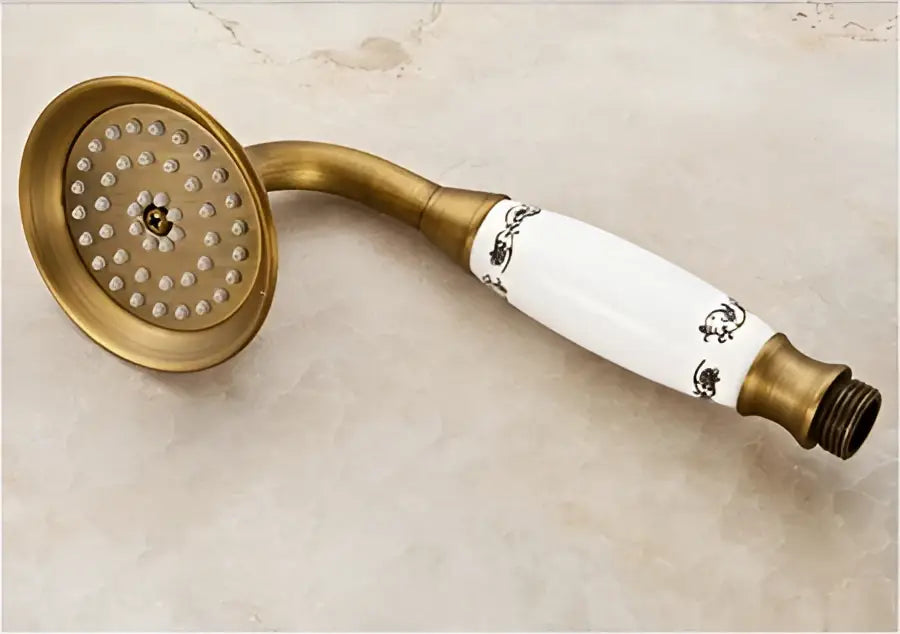 Antique brass shower set featuring a showerhead with white ceramic handle decorated with black floral patterns by DecorBites