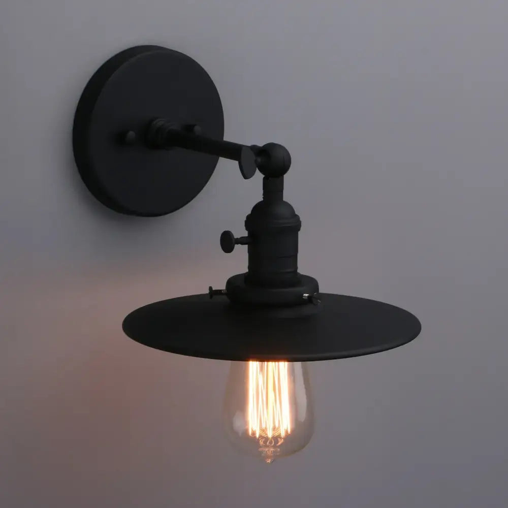 Black industrial wall sconce with antique finish, adjustable arm, wide shade, and clear filament bulb by DecorBites