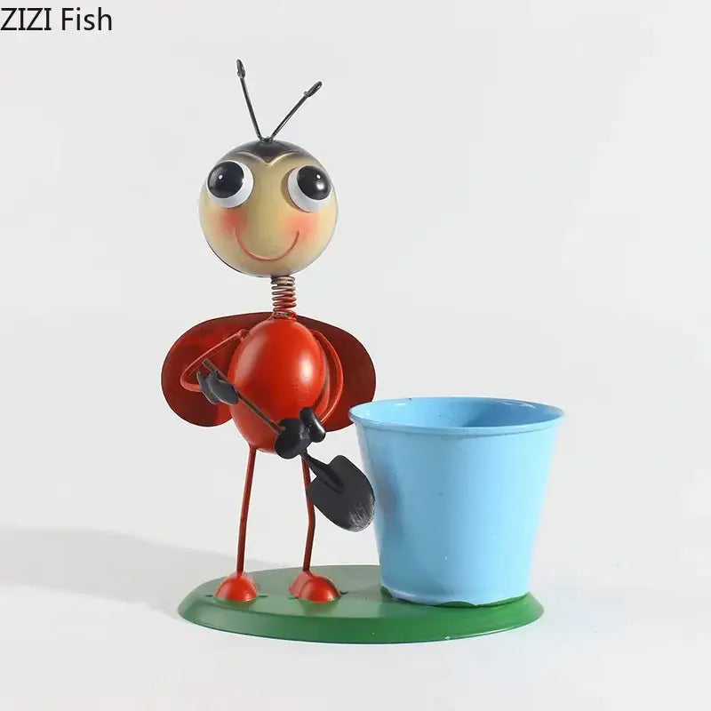 Red metal bee figurine with black antennae holding shovel next to light blue pot in DecorBites ants gardener vase