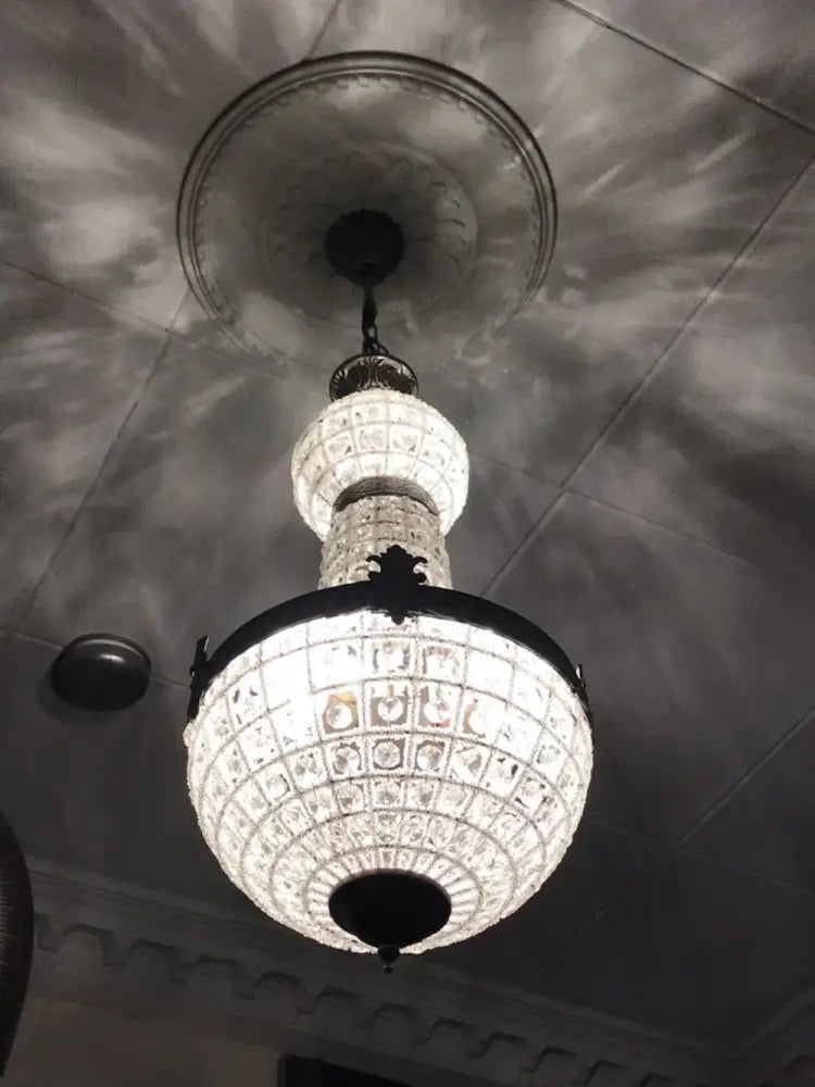 An ornate decorbites art deco crystal led chandelier with black metal frame and intricate cut-glass panels suspended from ceiling medallion