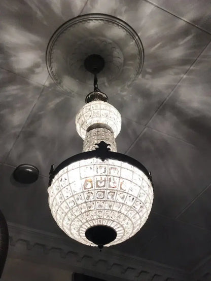 An ornate decorbites art deco crystal led chandelier with black metal frame and intricate cut-glass panels suspended from ceiling medallion