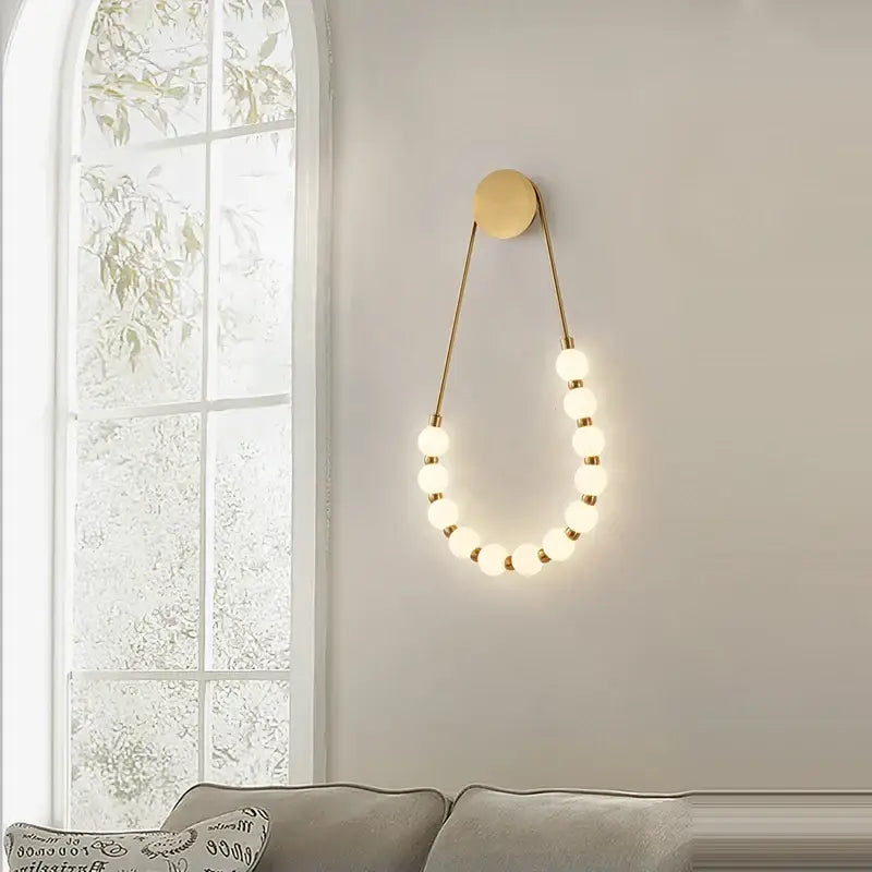 Gold-toned led wall sconce with circular base and glowing glass bulbs on slender metal wires for bedroom lighting