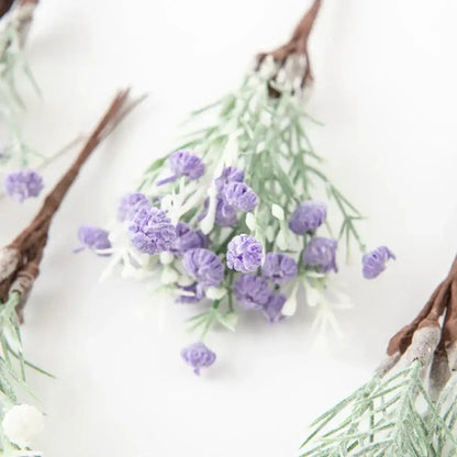 A delicate cluster of artificial gypsophila plants with soft purple blooms and pale green stems on rustic brown twig