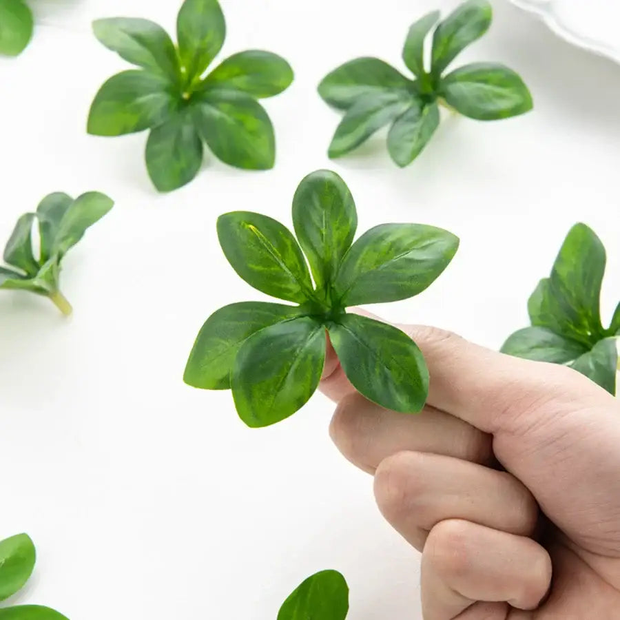 A hand holds a small green decorbites artificial rose leaf with five glossy veined petals for DIY wreaths