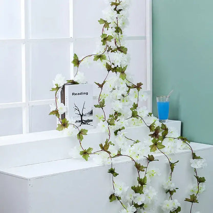 A delicate white decorbites artificial sakura flowers vine with green leaves for indoor or outdoor wedding decoration