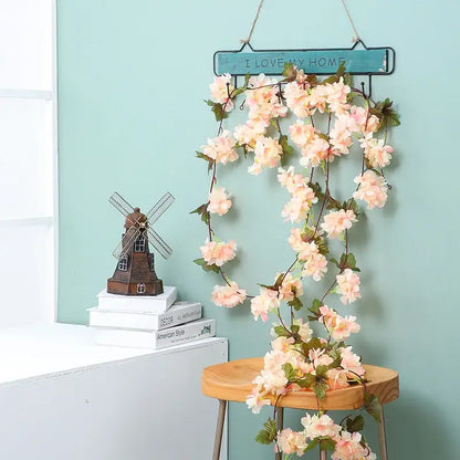 A delicate peach-colored decorbites artificial sakura flowers vine with green leaves hanging from a rustic teal sign