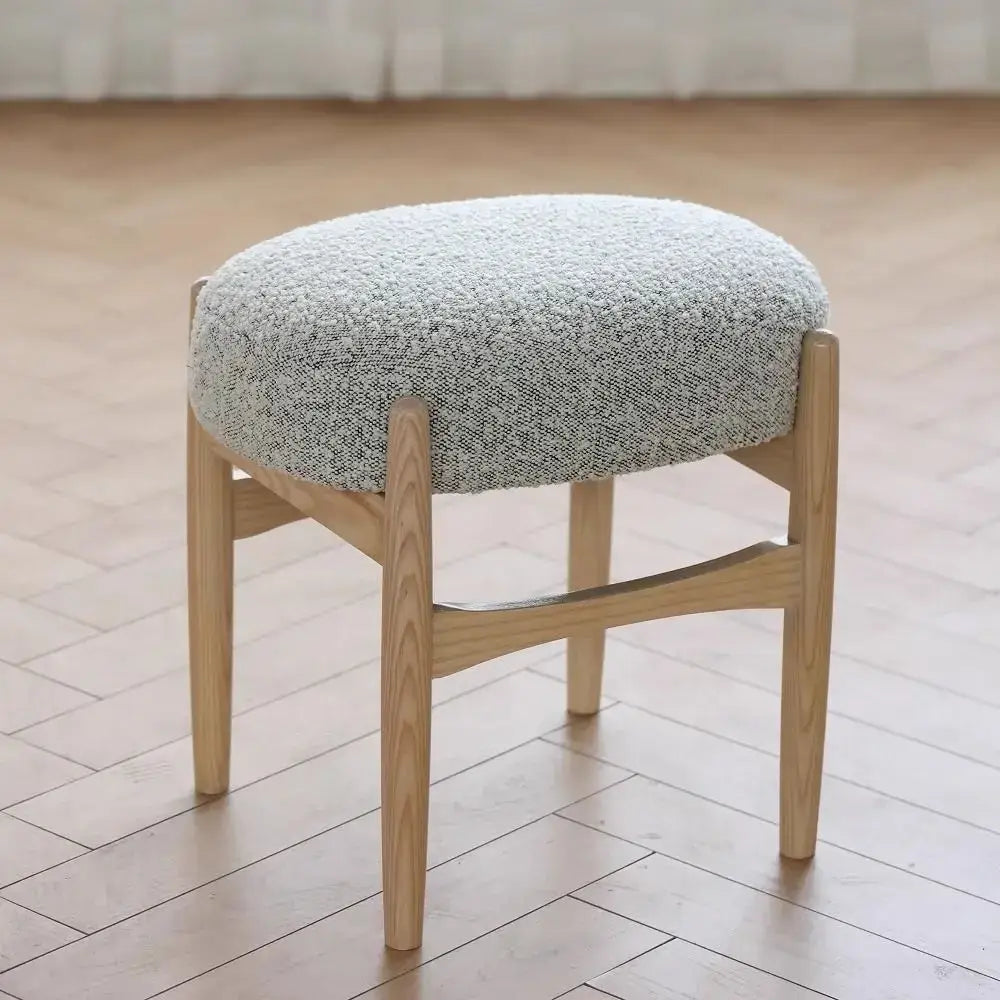Light gray textured fabric cushioned decorbites ash wood makeup bench with slender light wood legs for small spaces