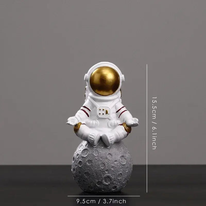 Decorbites astronaut figurine abstract sculpture in white with gold helmet seated in meditation on textured gray moon surface