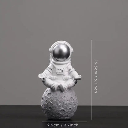 White astronaut figurine with metallic silver helmet seated in meditation pose on textured gray moon surface decorbites astronaut