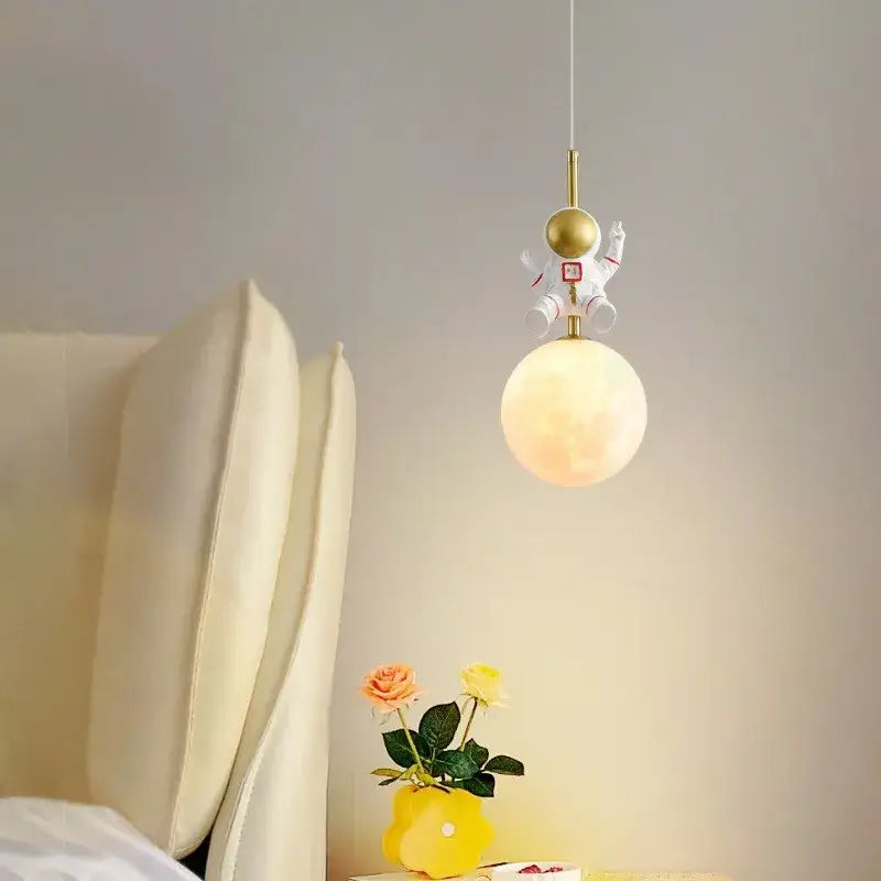 A whimsical white pendant light with gold accents from decorbites astronaut moon hangs above a glowing bedside globe