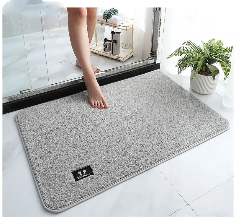 Gray plush decorbites bathroom mat with soft textured surface, subtle stitched border, and black embroidered logo patch