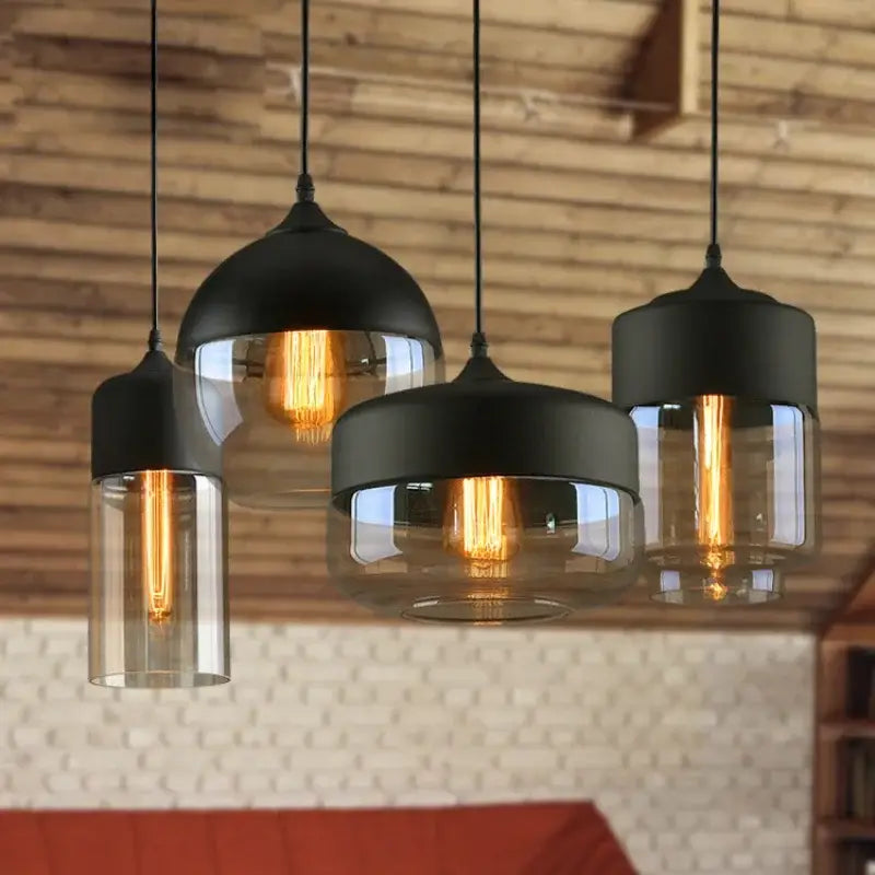 Set of four black glass pendant light fixtures with clear shades and exposed filament bulbs for modern indoor decor