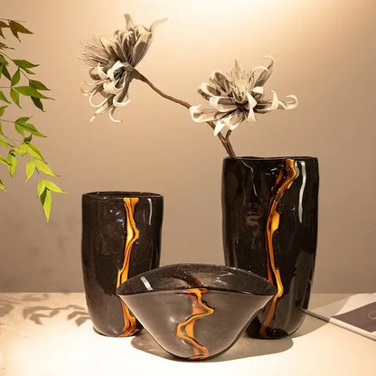 Set of three decorbites black glass vases with golden-orange marbled accents holding delicate white flowers for decoration