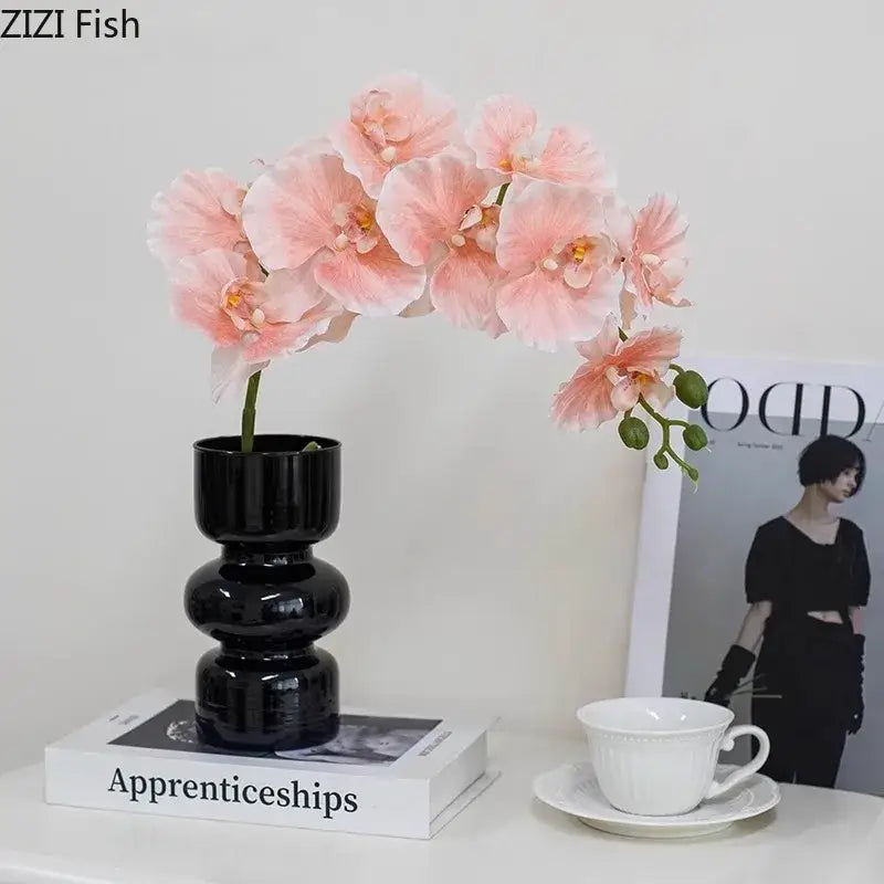 A decorbites black glass vase with stacked rounded segments holding delicate pink artificial flowers for stylish decor