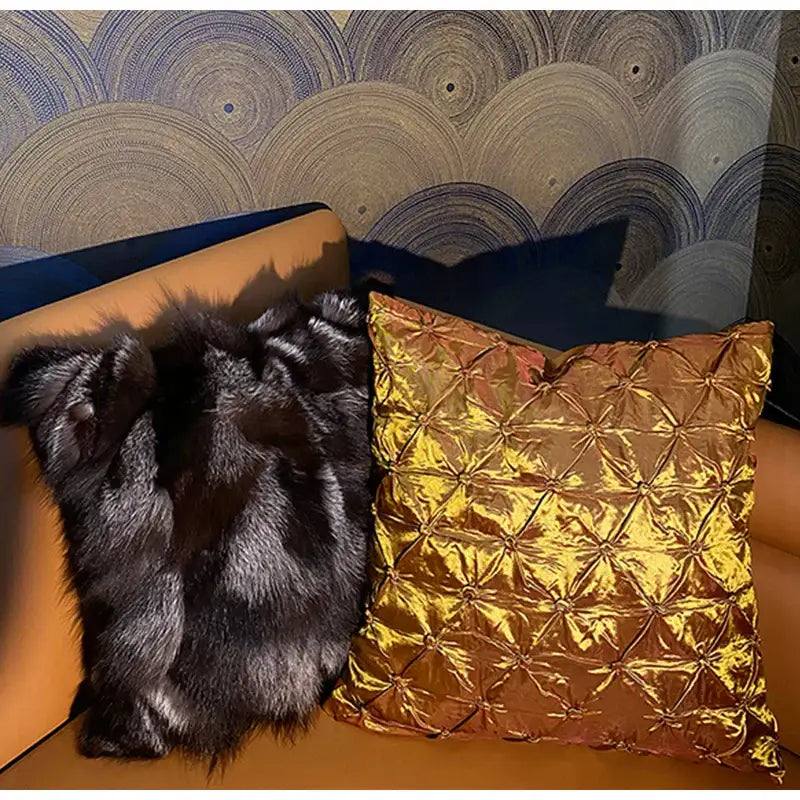 A luxurious gold-toned satin quilted throw pillow case next to a black faux fur throw on an orange couch