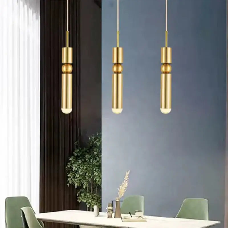 Three polished gold led tube pendant lights hang from the ceiling in the DecorBites black gold chandelier design