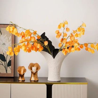 White textured ceramic vase with flared opening holding orange lantern flowers and black leaves from decorbites black gold resin handicrafts collection