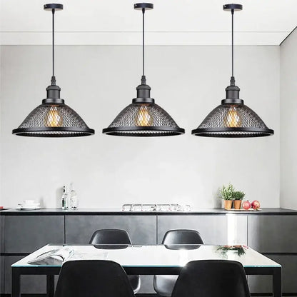 Three black iron decorbites pendant lights with mesh net-cage shades hang above a dining table for kitchen use