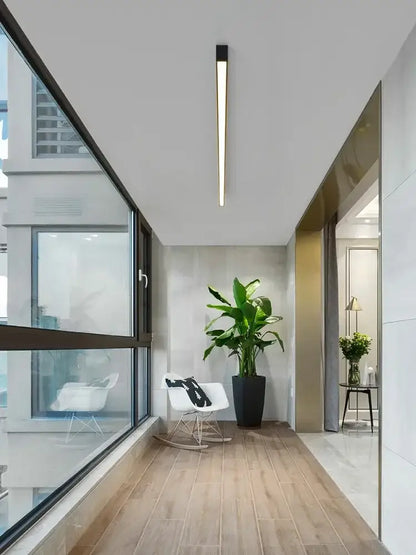 A sleek modern minimalist hallway illuminated by the decorbites black linear led ceiling lamp with a tall potted plant center