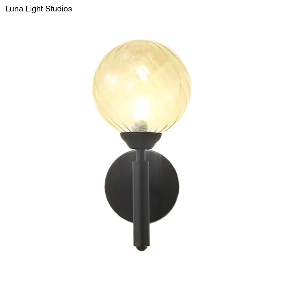 Modern black wall sconce with clear textured glass amber-toned spherical globe and black metal base for bedroom lighting