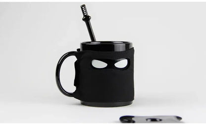 Decorbites black ninja mug with sword stirrer featuring glossy black finish and eye-shaped cutouts for kitchen novelty use