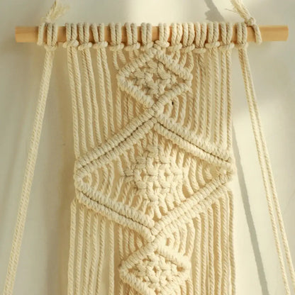 Cream-colored DecorBites™ boho macrame hanging shelf with geometric knotwork and natural wood dowel for home decor wall shelf