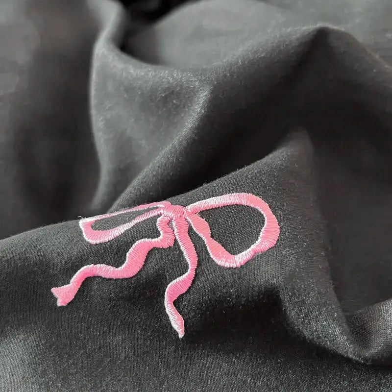 A delicate pink bow embroidery adorns dark fabric in the DecorBites™ bow embroidery bedding set with ruffles