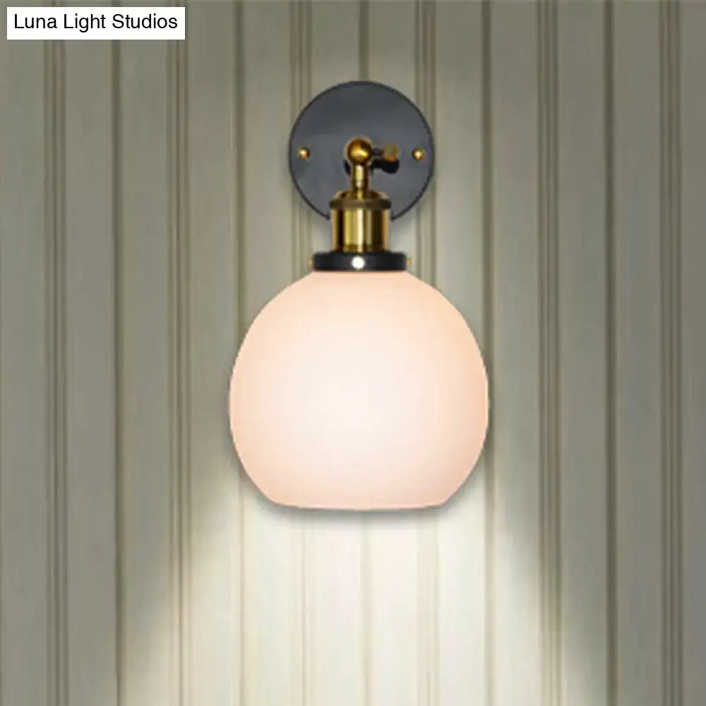 Industrial brass wall sconce with a soft pink bubble white glass globe and black mounting plate for bedroom use