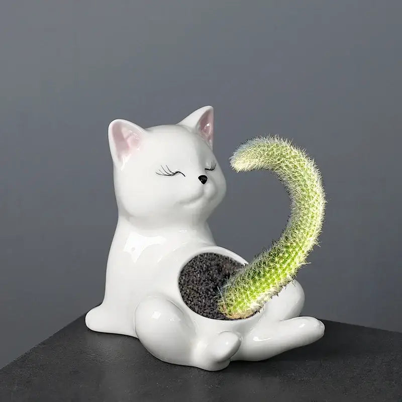 White ceramic decorbites cartoon kitten flowerpot with closed eyes and pink ears holding a curved green cactus plant