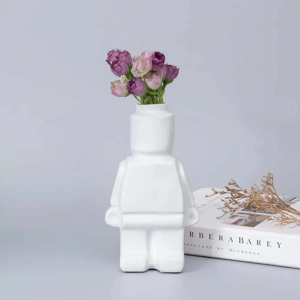 White ceramic robot vase shaped like lego minifigure holding purple and pink flowers nordic style decor