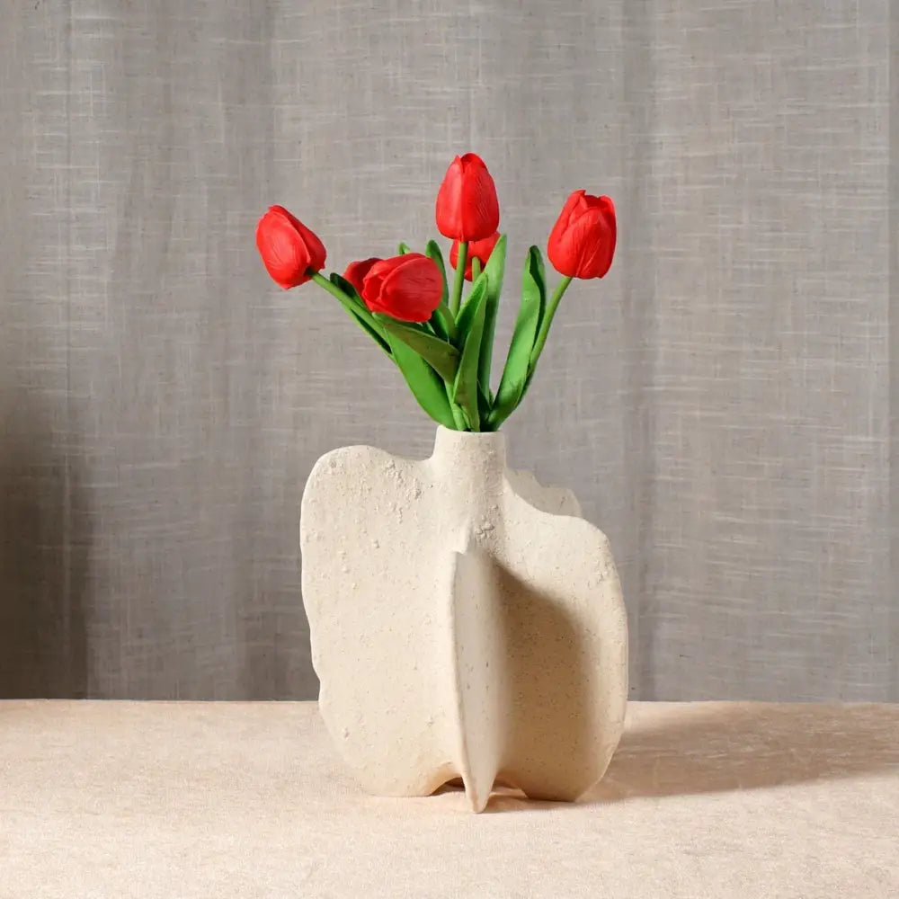 Cream-colored textured ceramic sea vase with organic sculptural form holding vibrant red tulips in nordic modern style
