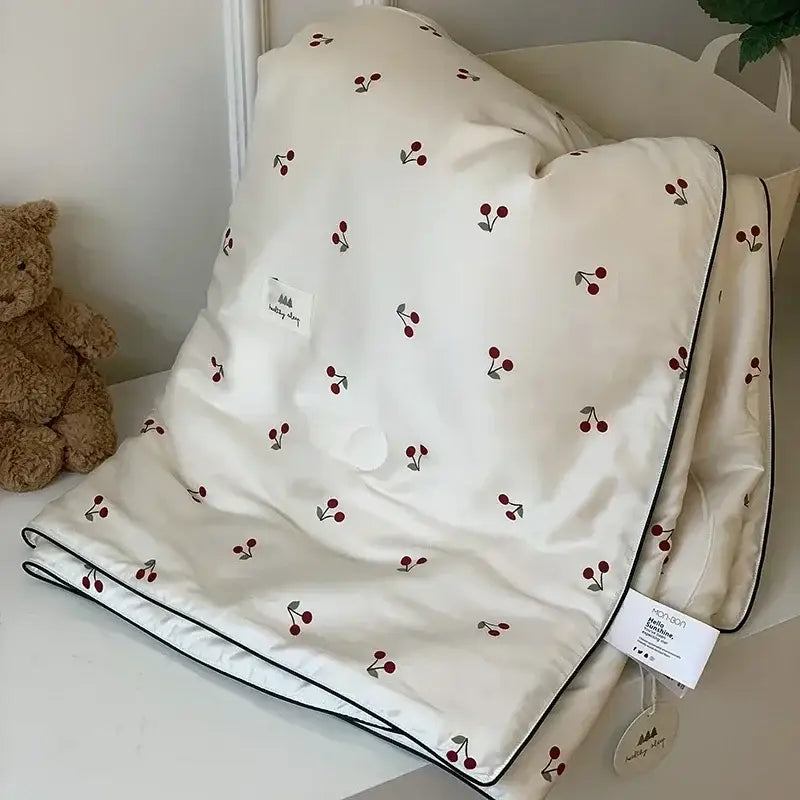 Cream-colored DecorBites cherry lyocell fiber cooling blanket with red green cherry pattern and black piping edges