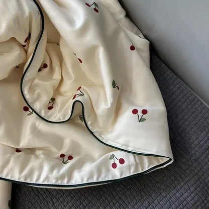 Cream-colored decorbites cherry lyocell fiber cooling blanket with embroidered red cherries and dark green piping edges