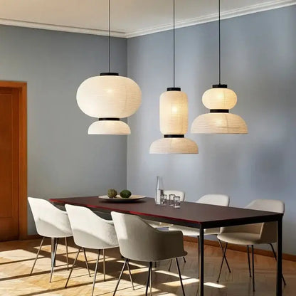 Three modern decorbites pendant lights with paper lantern shades and black metal fixtures hanging above a dining table
