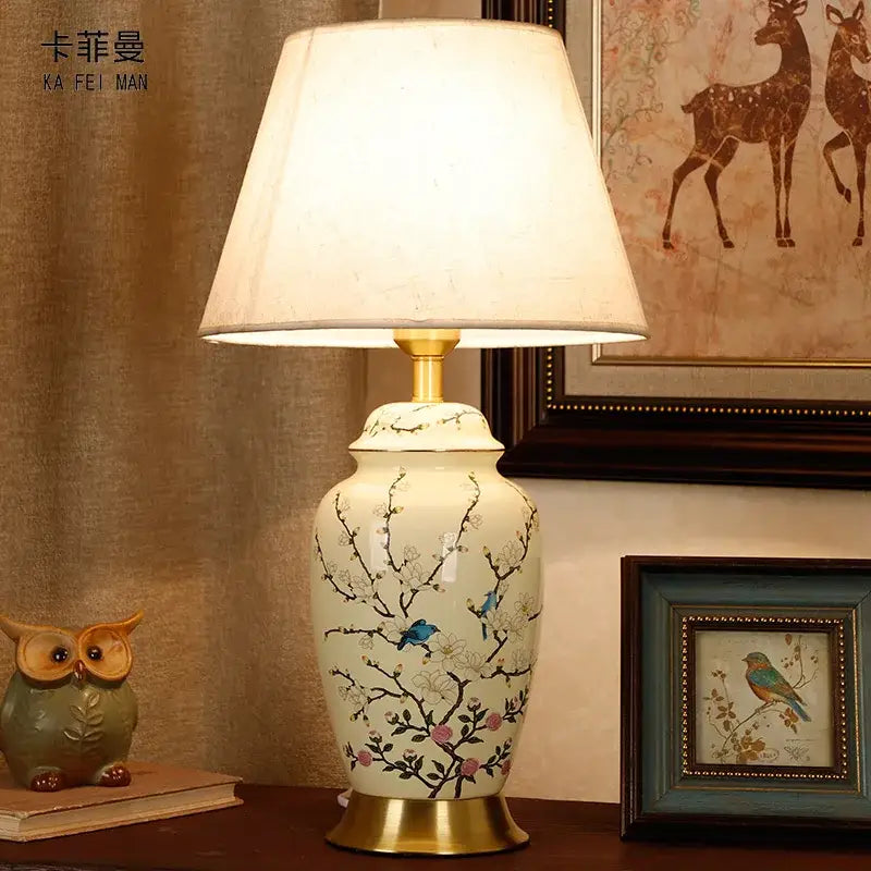 Cream-colored ceramic table lamp with hand-painted blue birds and pink blossoms on gold-toned base by DecorBites