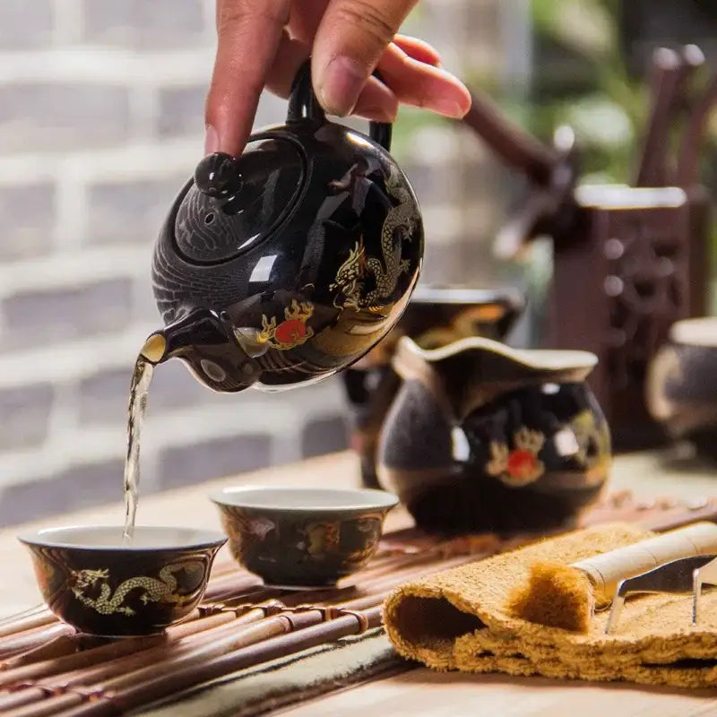 Black ceramic red tea pot with gold dragon and red floral designs being poured in DecorBites™ tea set